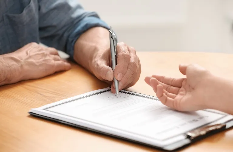 Two people interacting over a clipboard with a document, one holding a pen poised to write.