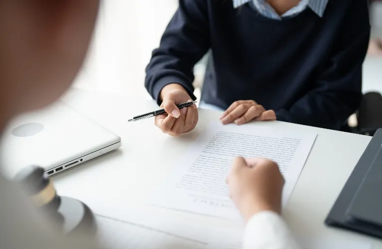 Two individuals in a professional setting reviewing a printed document at a white desk.